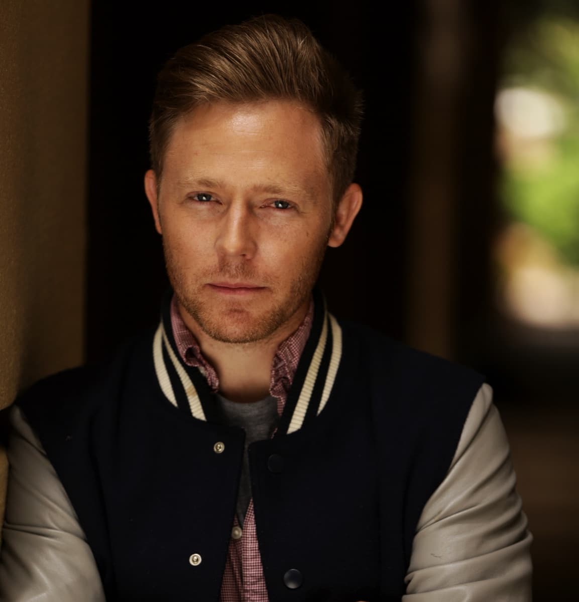 Brandon Selfors, close up and unsmiling, in a navy varsity jacket with cream leather sleeves over a checked shirt